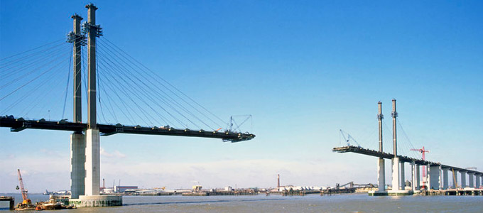 Eine große Brücke im Bau in einer Hafenstadt vor blauem Horizont, welche einen Brückentag symbolisieren soll.