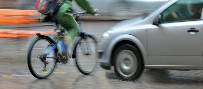 Eine Unfallsituation mit Fahrrad und Auto auf einer Straße. Das Auto droht mit dem Fahrrad zu kollidieren. Das Foto ist stark geblurrt, um die Geschwindigkeit beider Verkehrsteilnehmer zu simulieren.