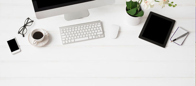 Minimalismus am Arbeitsplatz / auf dem Foto: Ein sehr aufgeräumter Büro-Arbeitsplatz mit Desktop-PC und den wichtigsten Arbeitsutensilien (Tablet, Bildschirm, Tastatur, Maus, Notizblock, Stift, Brille, Smartphone, Pflanze und eine Tasse Kaffee)