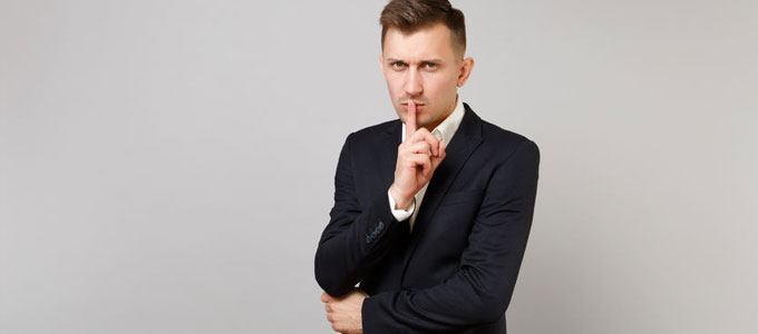 Ghosting im Bewerbungsverfahren Wenn der Arbeitgeber plötzlich schweigt / Auf dem Foto: Ein Mann symbolisiert mit seinem Zeigefinger vor seinem geschlossenen Mund Stille bzw. Schweigen und schaut entnervt.