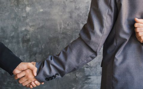 Toxische Kollegen: Giftspritzen im Job ausbremsen / auf dem Foto: Zwei Kollegen geben sich die Hand. Eine der Personen hält dabei hinterm Rücken ein Messer in der anderen Hand.