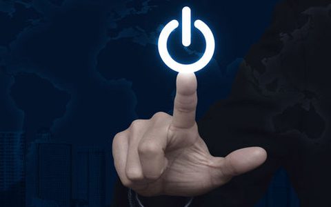 Abschalten nach Feierabend: Darum ist es so wichtig / auf dem Foto: Eine Person klickt mit ausgestrecktem Zeigefinger auf einen Ausschalt-Knopf (auch bekannt als Power Button). Im Hintergrund ist leicht schattiert eine Skyline aus Wolkenkratzern zu sehen, als auch die Weltkarte, als eine Art Wasserzeichen.