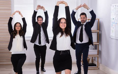 Betriebssport: Gut für Teambuilding und Fitness / auf dem Foto: Eine Gruppe von Kollegen führt gemeinsam Fitness/Streaching Übungen durch. Das Team wirkt dabei fröhlich und hat Spaß. Teambuilding durch Fitness.