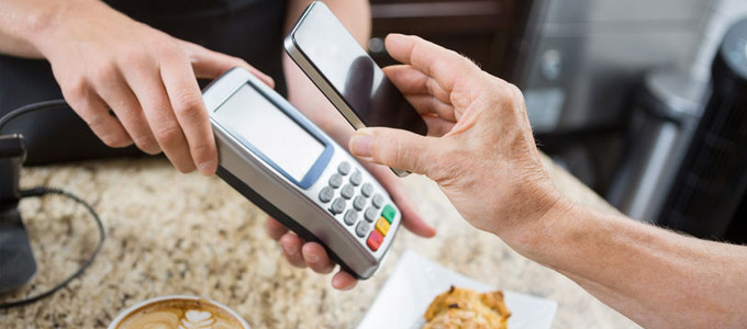 Zahlungsarten online und offline / auf dem Foto: Ein Kunde bezahlt seinen Kaffee und Kuchen mit dem Smartphone / Handy.