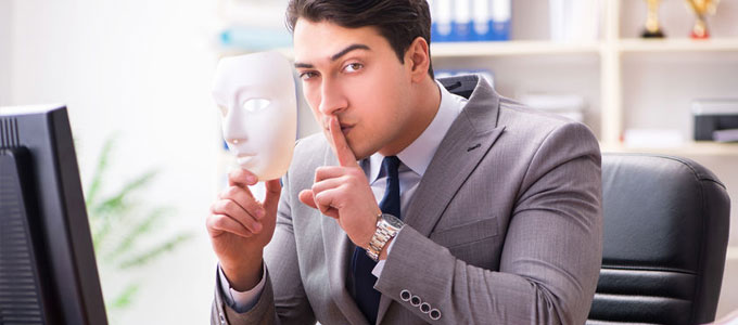 Ein Mann hält eine Maske in seiner Hand und den erhobenen Zeigefinger vor seinem Gesicht