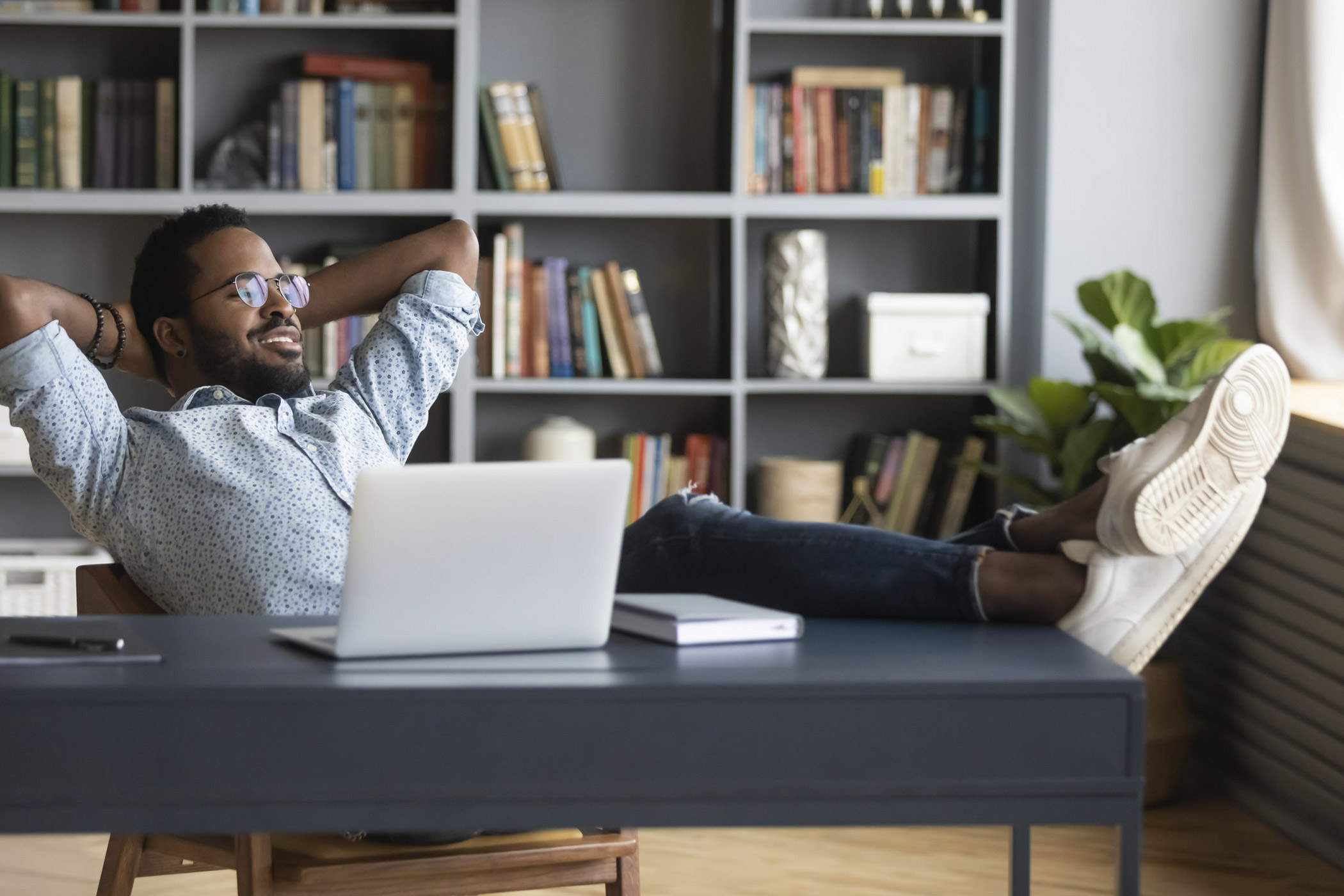 Abmahnung im Homeoffice: Was gilt? auf dem Foto: Mann, der sich am Schreibtisch zu Hause zurücklehnt, die Beine auf den Tisch legt und Pause macht
