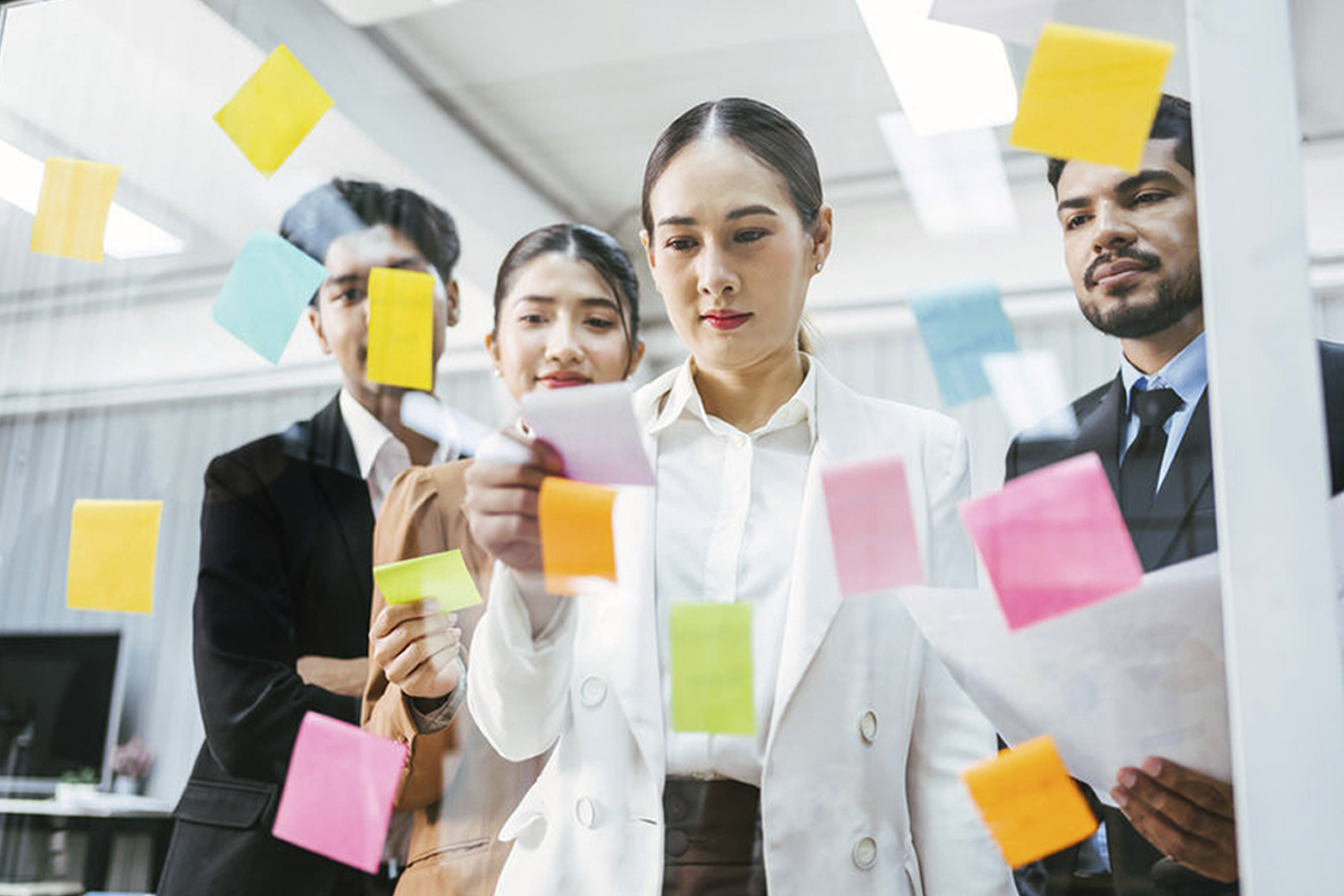 Haftnotizzettel und KI: Was im Büro noch analog ist auf dem Foto: Mitarbeitende, die vor bunten Haftnotizzetteln an einer gläsernen Wand stehen
