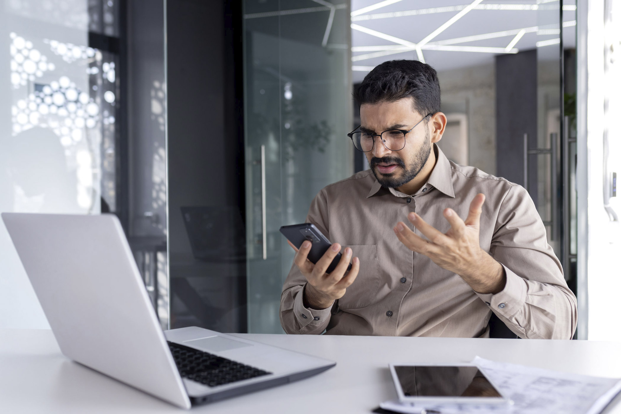 Wenn die Technik streikt, ist das erstmal ärgerlich und frustrierend. Auf dem Foto: Mann am Schreibtisch, der wütend auf Handy und Laptop schaut