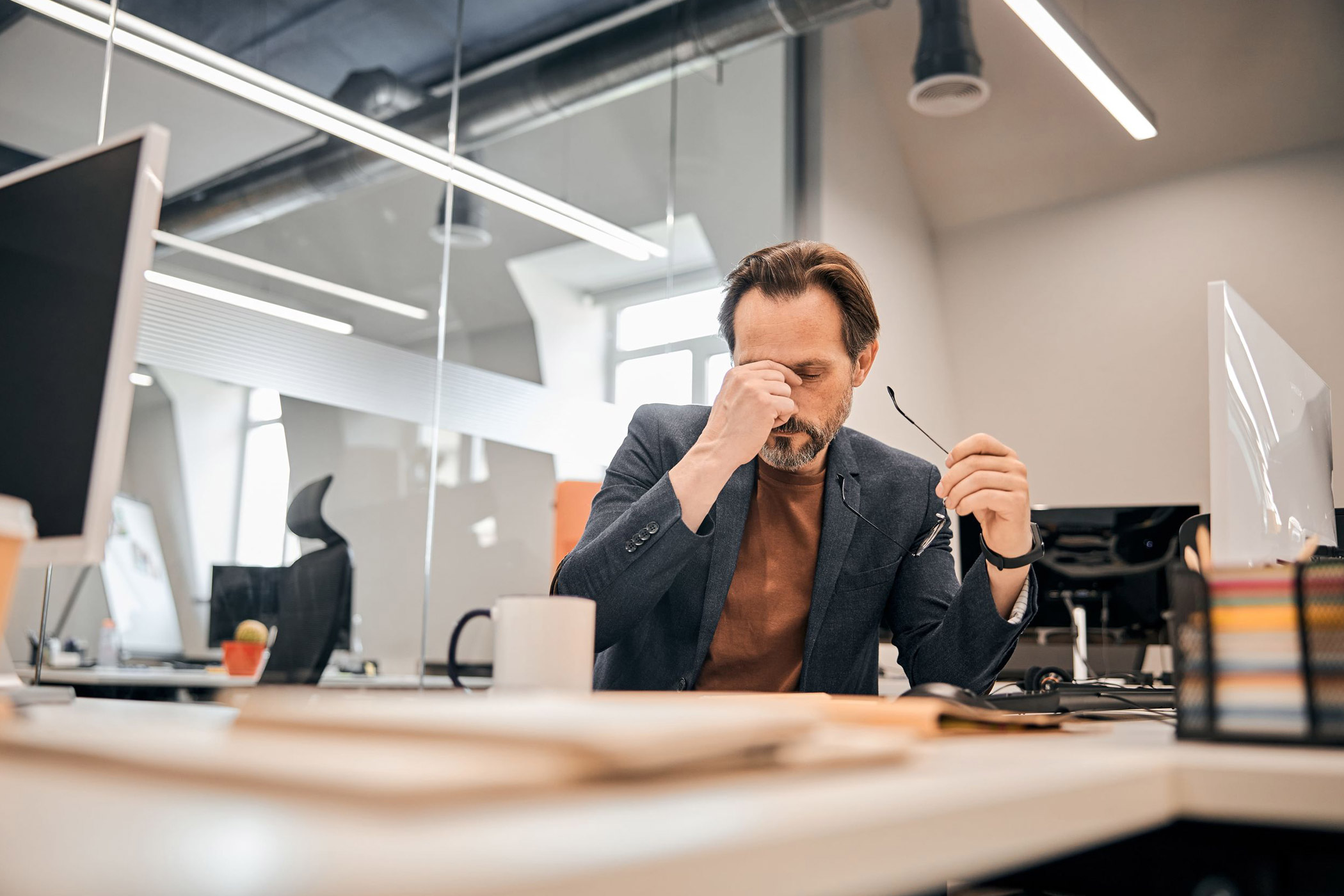 Bei dicker Luft im Büro kann auch die Konzentration leiden. Auf dem Foto: Ein Angestellter, der seine Brille abgenommen hat und sich erschöpft ins Gesicht fasst